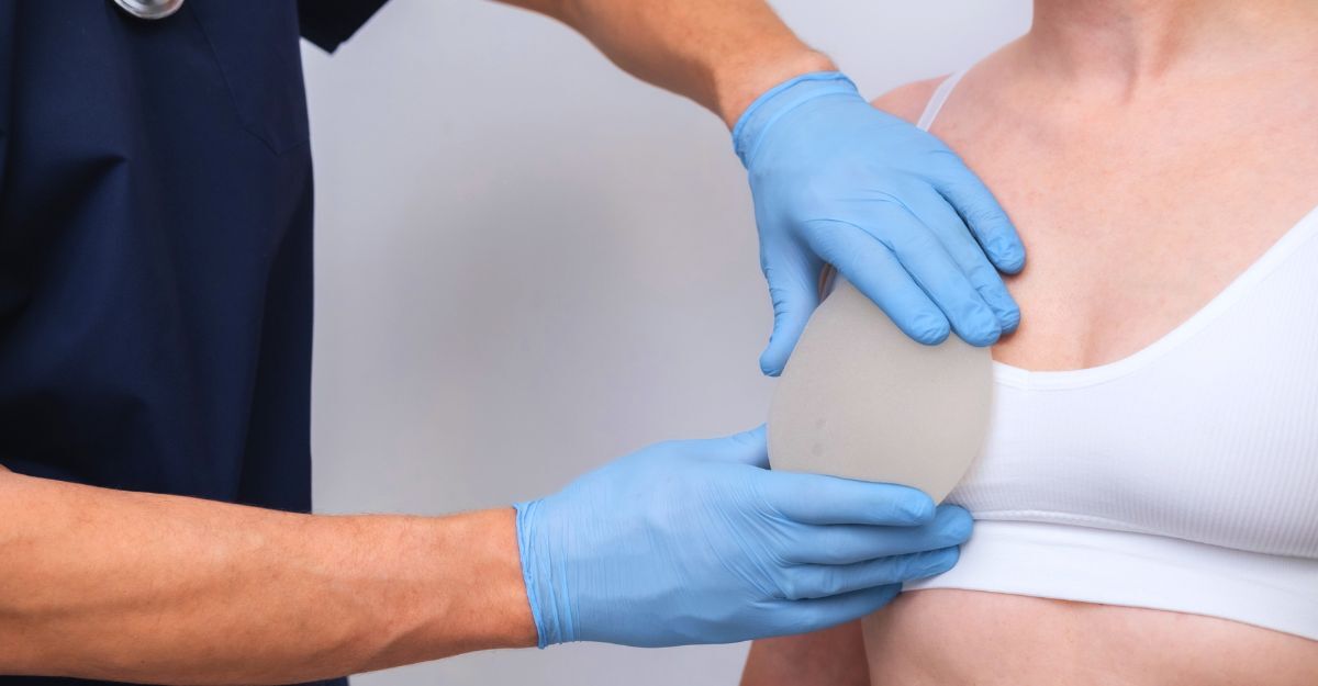 Primo piano di un chirurgo coi guanti che prova una protesi sul seno di una cliente coperto da un top sportivo