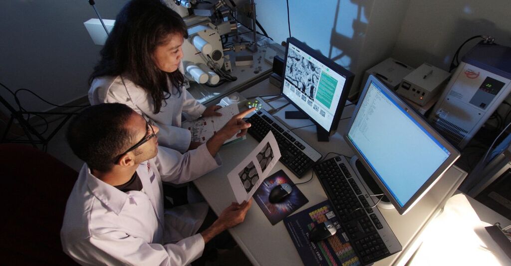 Vista dall'alto di due scienziati in camice da laboratorio che esaminano dati e immagini al computer.