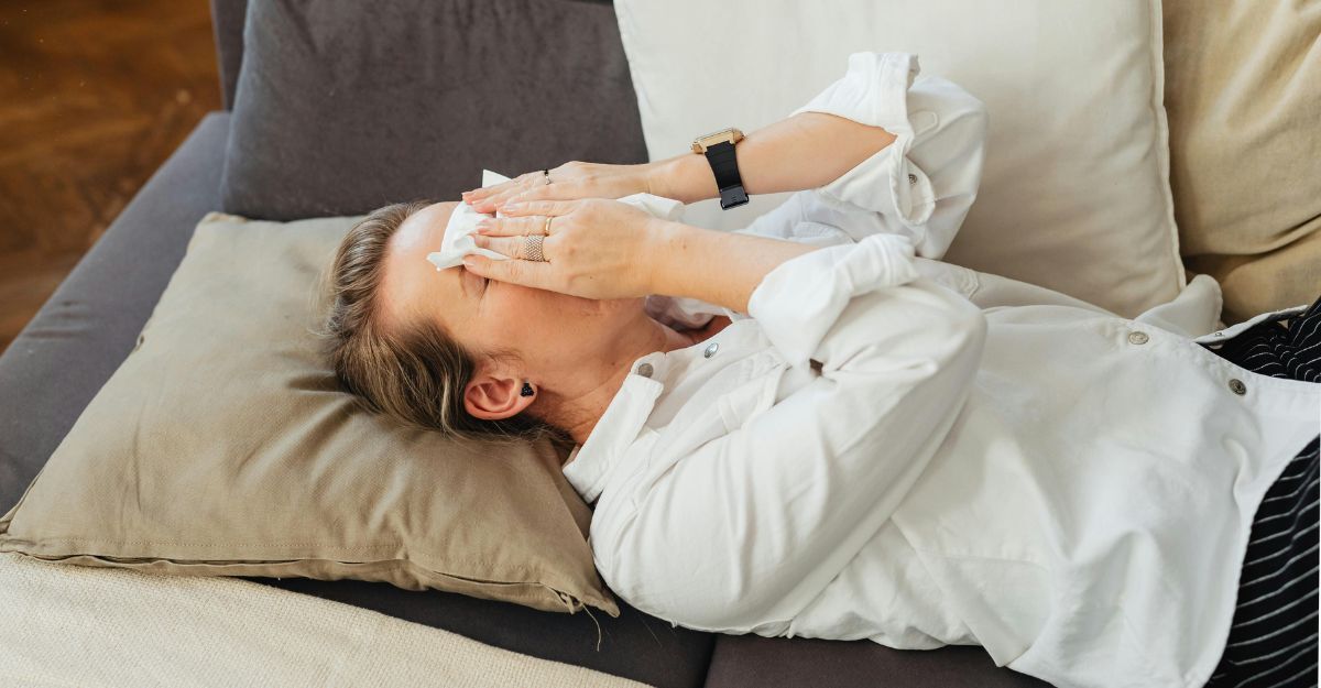 Donna sdraiata sul divano con gli occhi chiusi e le mani che tengono un fazzoletto sul naso