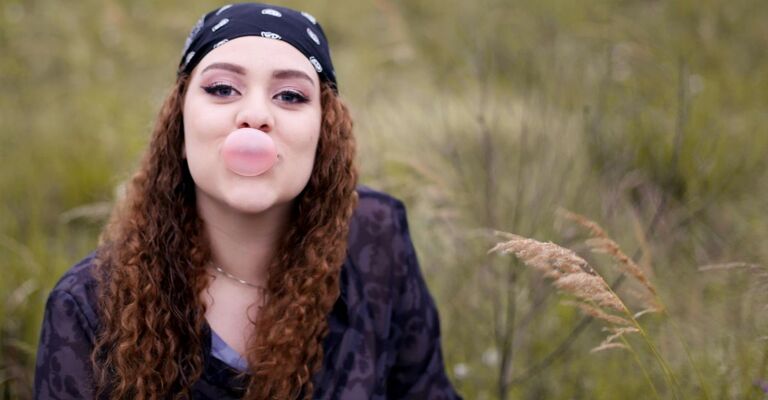 Giovane donna che mastica una gomma da masticare con dolcificanti artificiali e fa una bolla