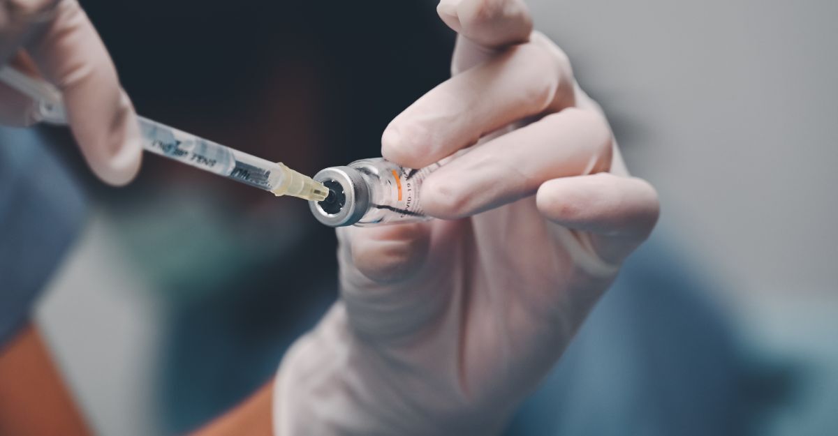 Primo piano di un flacone di vaccino da cui una siringa con ago estrae il liquido.