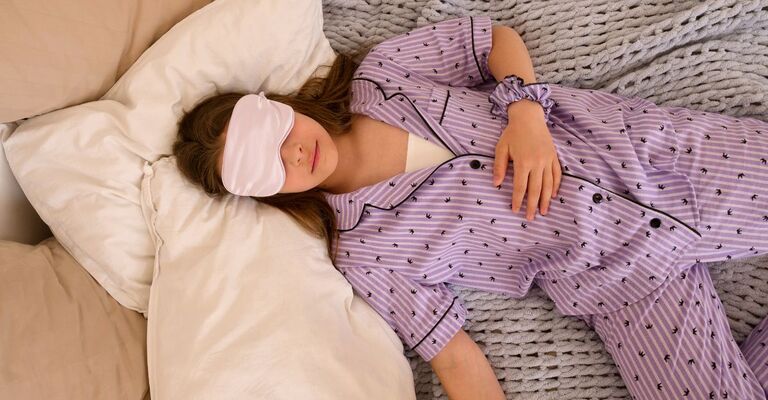 ragazza in pigiama lilla dorme nel letto, con la mascherina per gli occhi