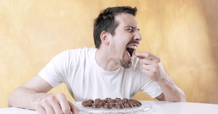 Un uomo mangia davanti a un piatto di cioccolatini.