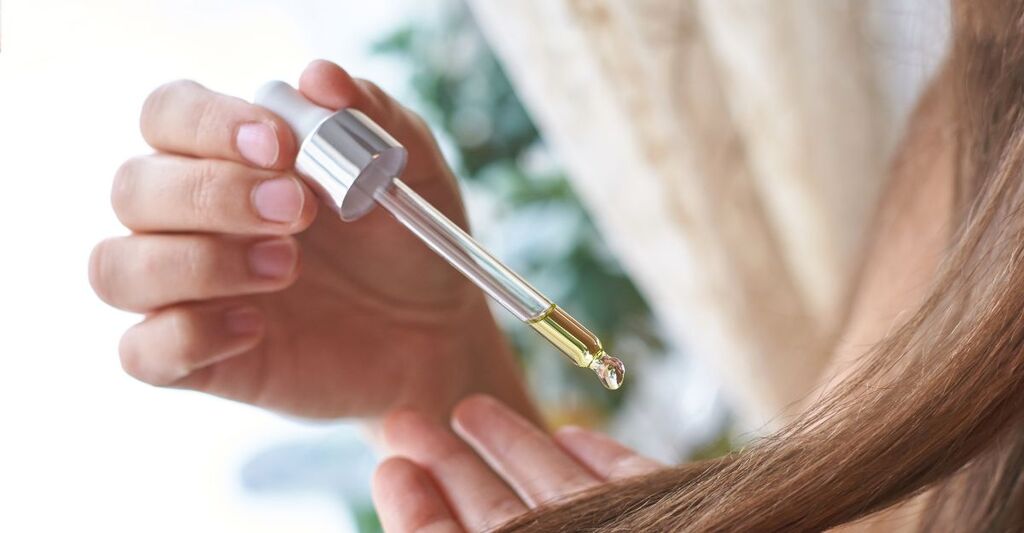 Ragazza che applica olio per capelli con un contagocce su una ciocca di capelli lunghi e lisci