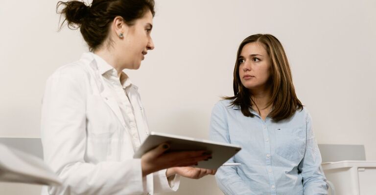 Paziente che discute con la ginecologa durante una consulenza medica, mentre la dottoressa prende appunti su un tablet.