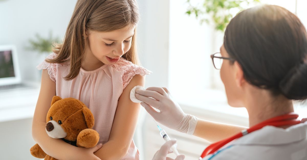 Una bambina con in braccio un orsacchiotto guarda un'infermiera che le sta per fare una puntura al braccio.