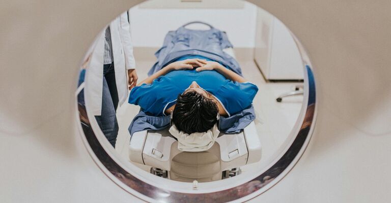 Paziente sdraiato sul lettino mentre entra nel macchinario della risonanza magnetica, accompagnato da un medico.