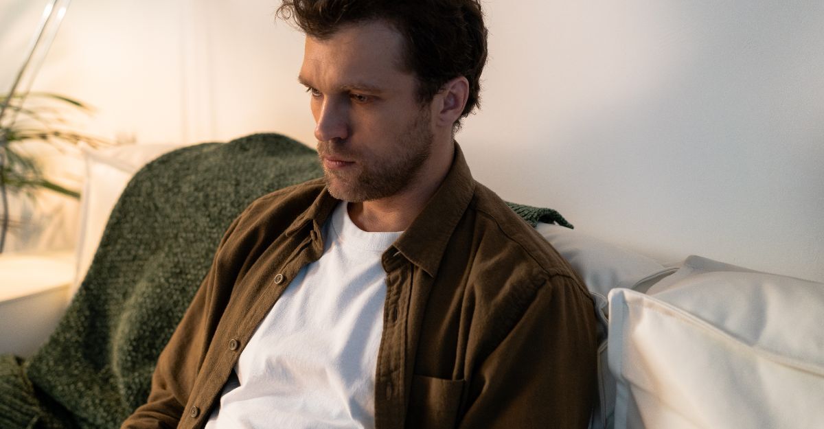 Primo piano di un uomo seduto su un divano con un'espressione pensierosa e preoccupata.