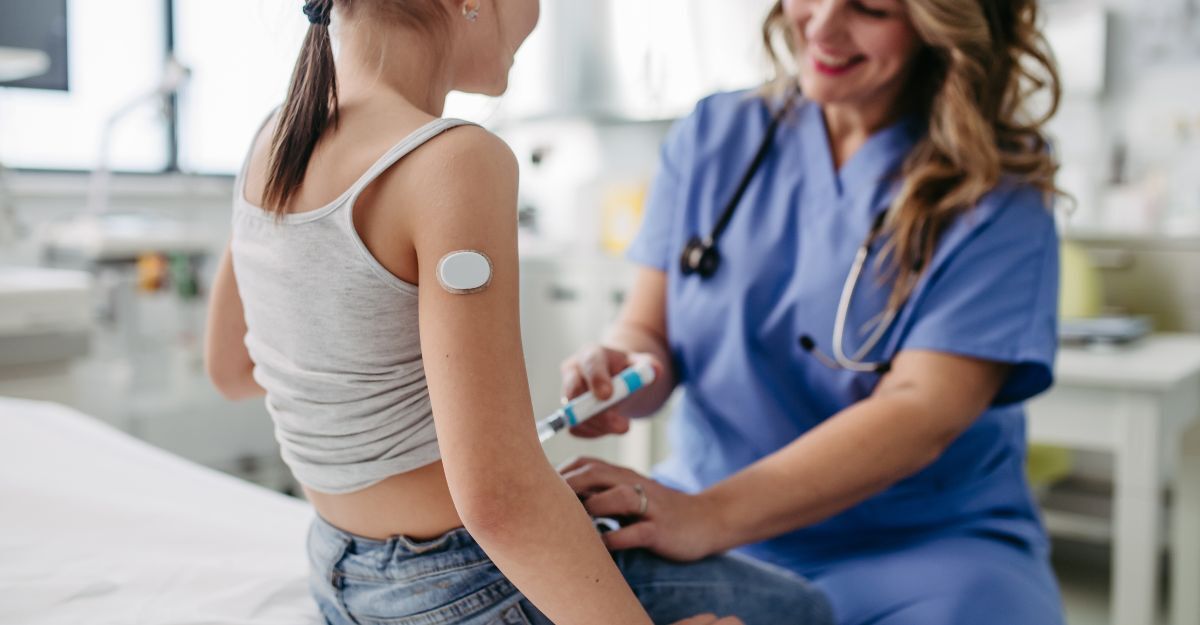 Primo piano di un medico che sorride a una ragazza seduta, con un sensore di glucosio attaccato al braccio.