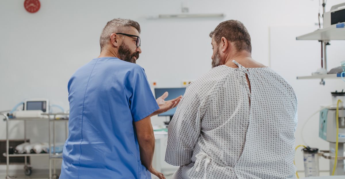 Medico in camice blu parla con un paziente obeso in camice ospedaliero durante una visita clinica.