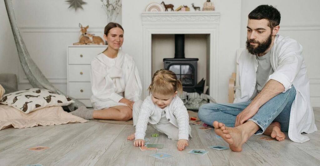 Neonata che gattona sul pavimento vicino ai due genitori e a delle carte per imparare nella sua cameretta