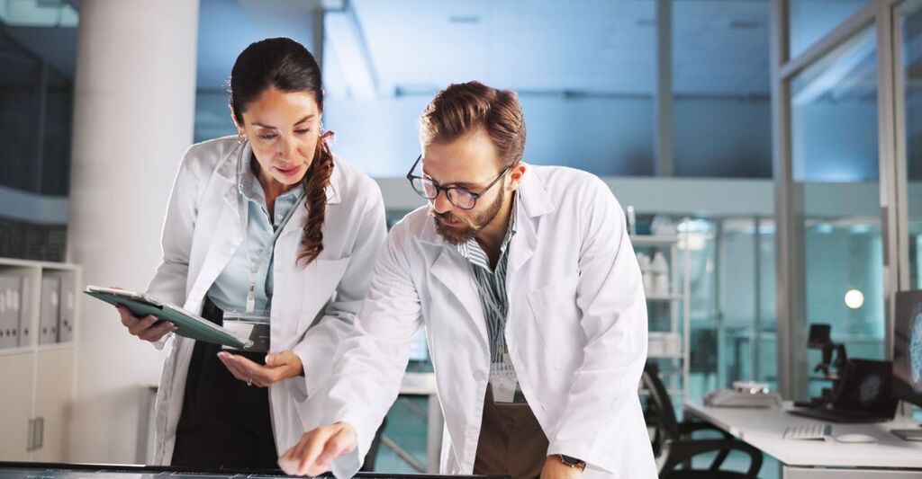 Due scienziati con camice in laboratorio che stanno controllando insieme uno studio