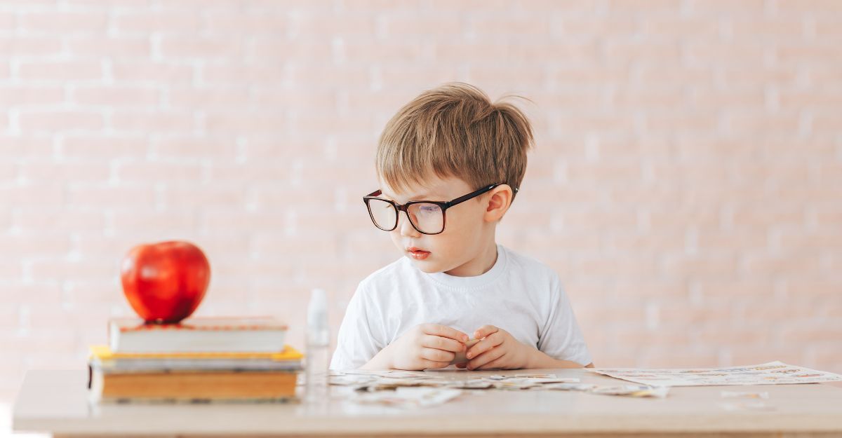 Un bambino con gli occhiali siede a un tavolo con una mela e dei libri.