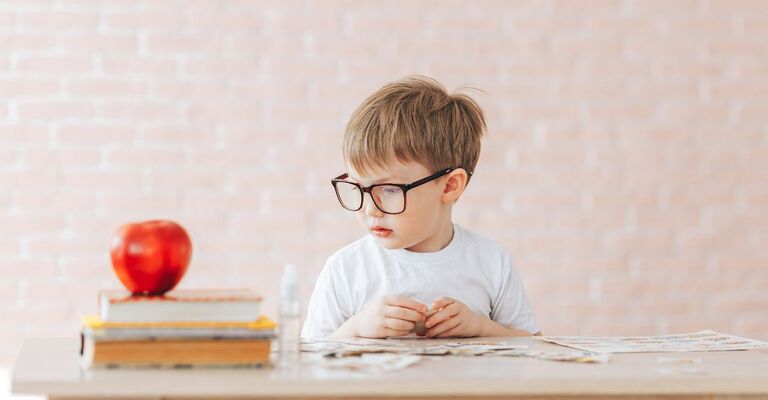 Un bambino con gli occhiali siede a un tavolo con una mela e dei libri.