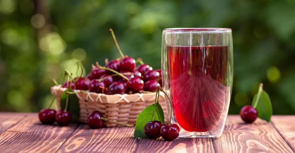 Una ciotola di ciliegie e un succo di ciliegia su un tavolo.