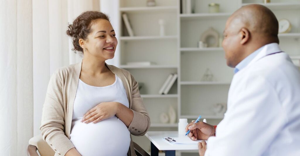 Primo piano di donna incinta sorridente e con la mano sul pancione mentre parla col suo ginecologo