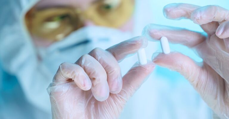 Primo piano di due mani con i guanti trasparenti di un ricercatore che tengono in mano due pillole