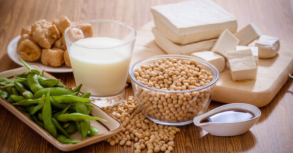 Una foto con varie forme della soia, come edamame, salsa di soia, tofu, latte di soia su un tavolo di legno