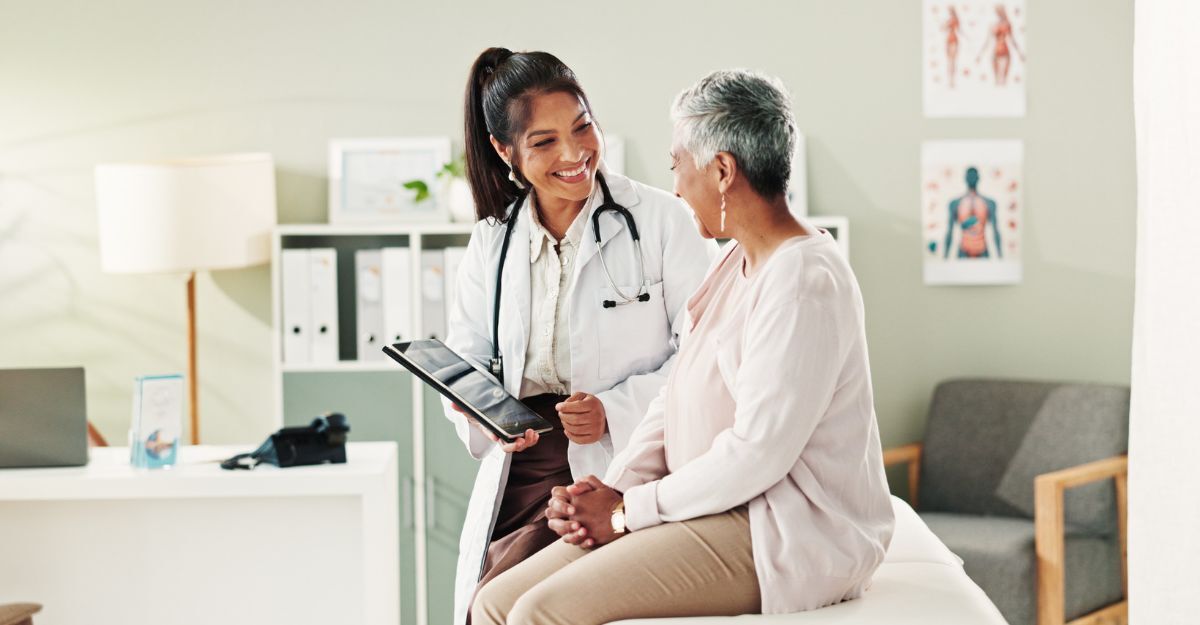 Primo piano di giovane dottoressa sorridente che mostra la cartella clinica alla sua paziente seduta sul lettino