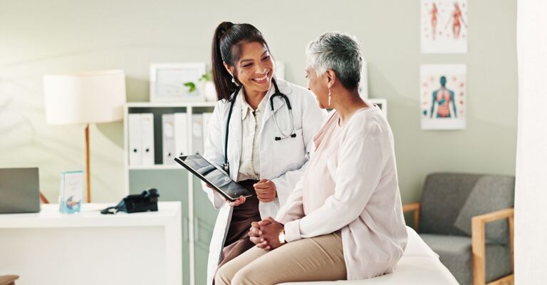 Primo piano di giovane dottoressa sorridente che mostra la cartella clinica alla sua paziente seduta sul lettino