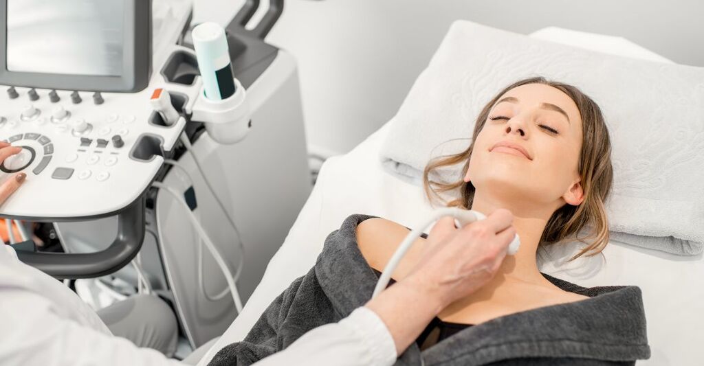 Una paziente è sdraiata su un lettino durante un'ecografia al collo (probabilmente alla tiroide)