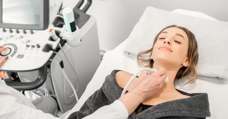 Una paziente è sdraiata su un lettino durante un'ecografia al collo (probabilmente alla tiroide)