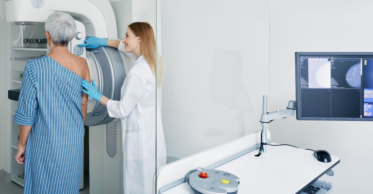 Una tecnica sanitaria, sorridente e con camice e guanti, assiste una paziente anziana durante una mammografia