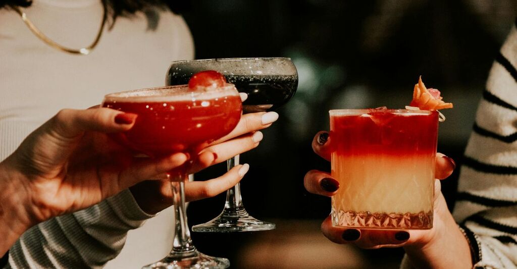 Mani che reggono e brindano con cocktail colorati.