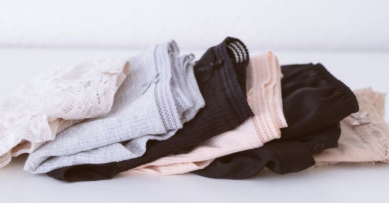 Pila di diverse mutandine da donna disposte su un tavolo bianco, di colore beige naturale. Sfondo di biancheria intima femminile.