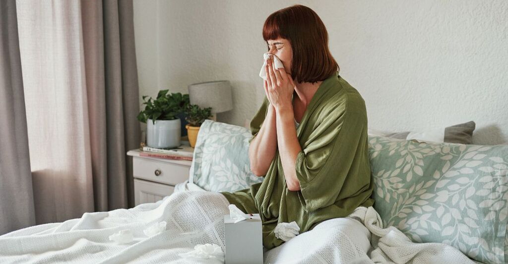 Donna, che si soffia il naso ed è malata a casa, con allergie e fazzoletti per malattie o raffreddore o influenza in camera da letto. Persona di sesso femminile, sinusite e guarigione da virus o febbre da fieno, a letto e infezione da influenza o Covid