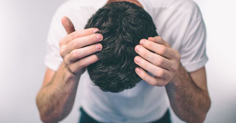 Uomo visto dall'alto che si tiene la testa, mostrando capelli scuri con alcuni fili bianchi.