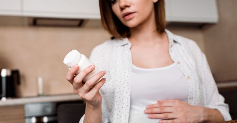 Primo piano selettivo di una donna incinta che guarda una bottiglia di vitamine