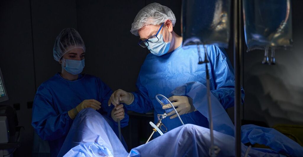 Ginecologo con assistente donna in mascherina e cuffia per capelli, paziente sulla poltrona ginecologica. Intervento di isteroscopia