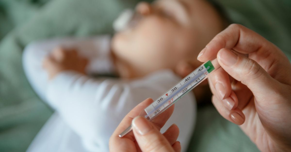 Mani di un adulto che tengono un termometro a mercurio con lo sfondo sfocato di un bambino sdraiato.