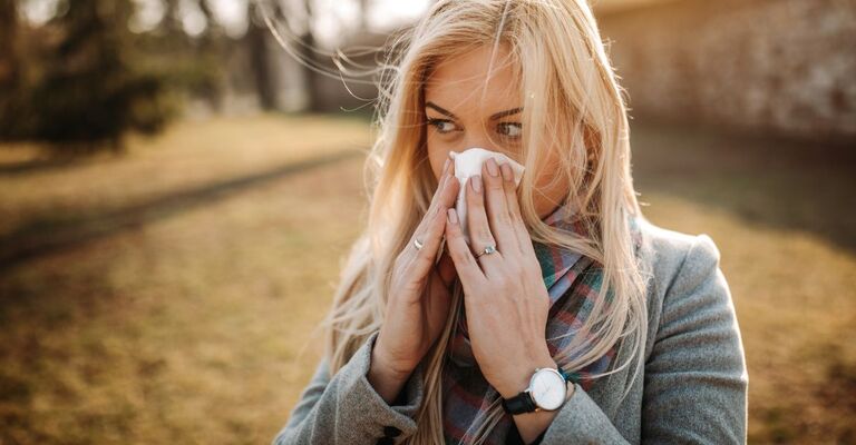 Donna bionda che si soffia il naso in un fazzoletto in un parco.