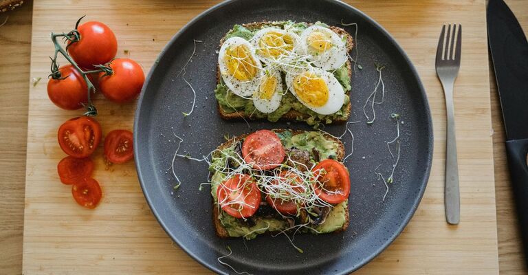Primo piano di un piatto color antracite con sopra due fette di pane tostato con sopra uova, avocado e pomodori