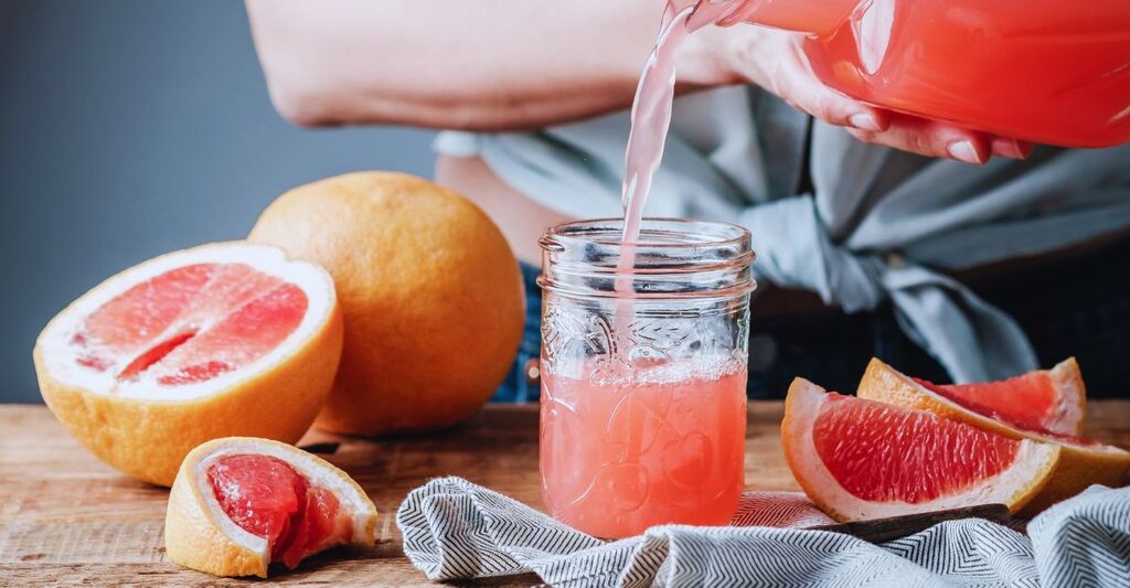 donna che versa il succo di pompelmo rosa da una brocca di vetro in un bicchiere da cocktail