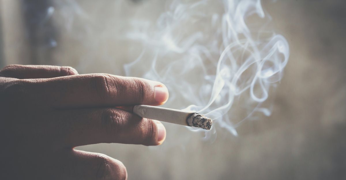 Mano che tiene una sigaretta accesa con fumo che si alza.