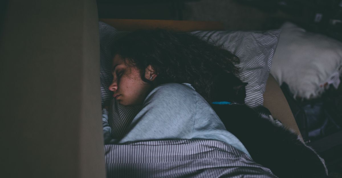 Donna che dorme abbracciata a un gatto nero in una stanza buia.