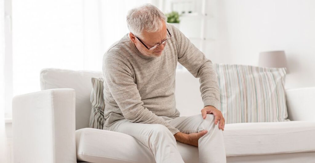 Un uomo sul divano  con dolore articolare al ginocchio.