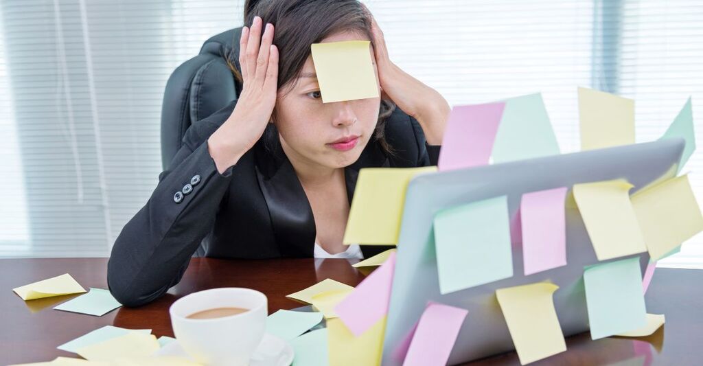 Una donna visibilmente stressata davanti al PC ricoperto di post it.