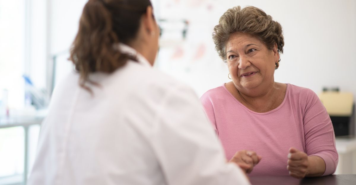 Donna anziana in rosa che parla con un medico in camice bianco.