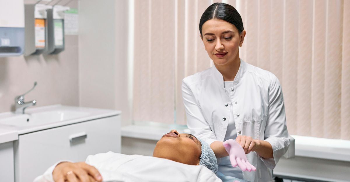 Primo piano di una dermatologa che si prepara a effettuare una visita con i guanti rosa alla paziente sdraiata sul lettino nel suo studio