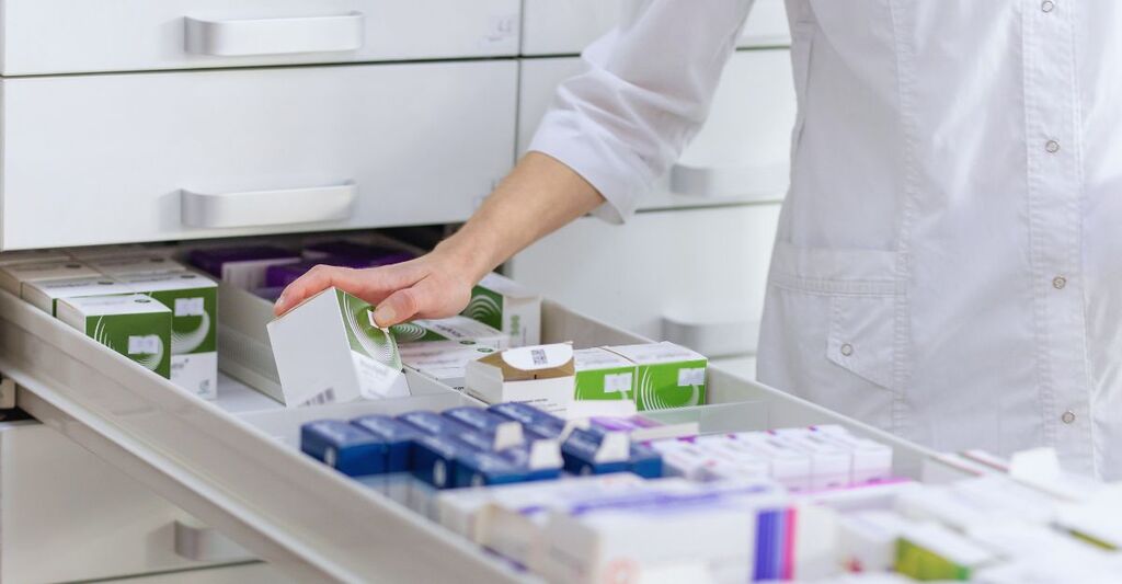 Farmacista che tiene in mano una scatola di medicinali e una confezione di capsule in una farmacia