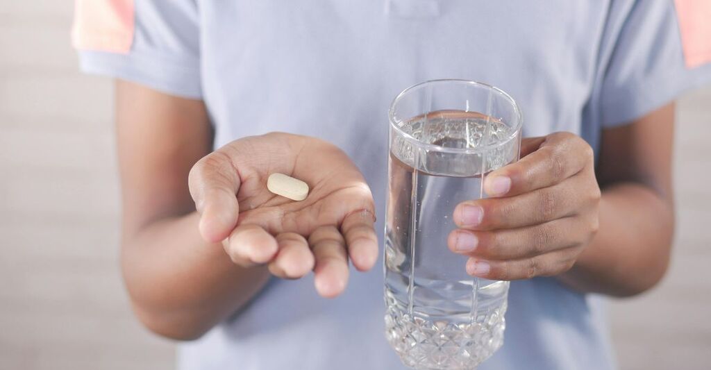 Persona con pillola e bicchiere d'acqua.