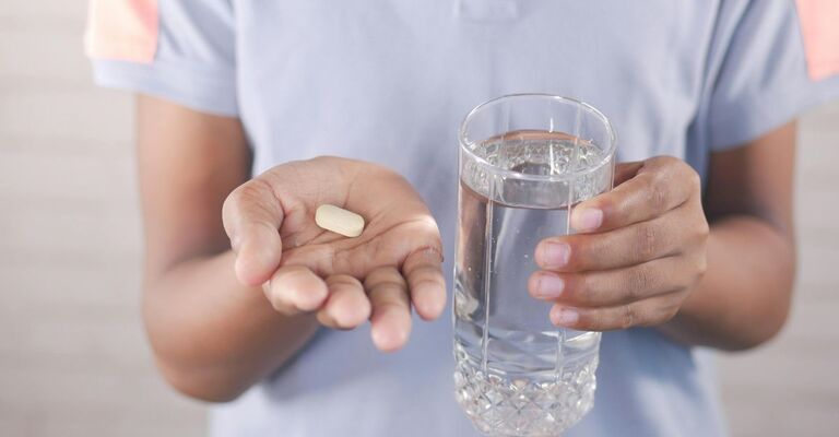 Persona con pillola e bicchiere d'acqua.