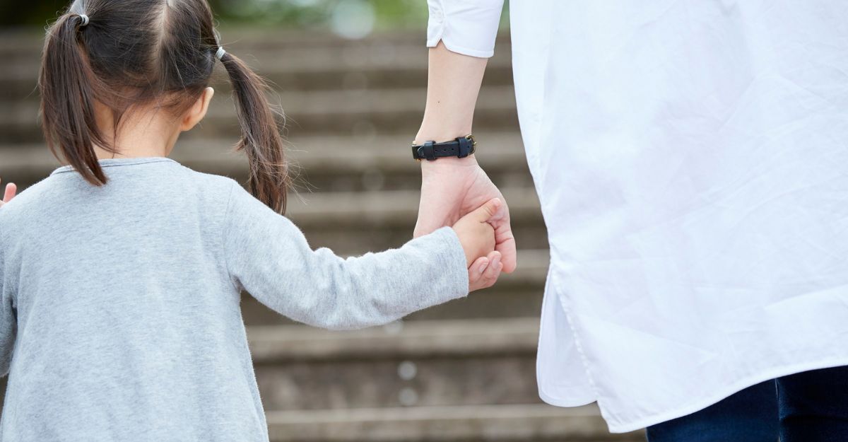 Primo piano di una bambina che tiene la mano di un adulto mentre salgono le scale.