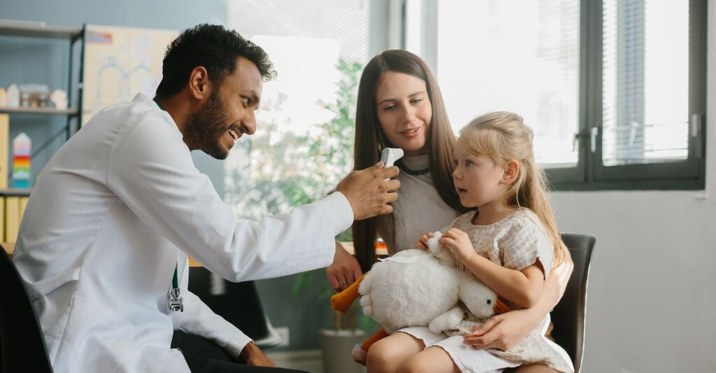Un giovane pediatra misura la temperatura a un piccolo paziente. Madre e figlia a una visita medica