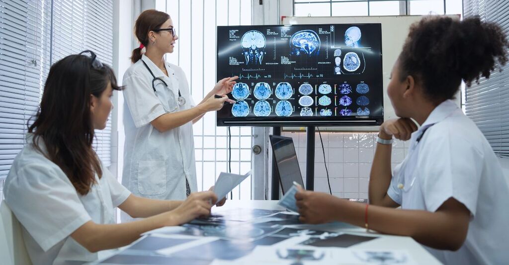 Un gruppo di scienziate mediche si riunisce in un laboratorio di ricerca sul cervello, davanti a un monitor che mostra immagini cerebrali ottenute tramite risonanza magnetica e TAC.