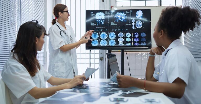 Un gruppo di scienziate mediche si riunisce in un laboratorio di ricerca sul cervello, davanti a un monitor che mostra immagini cerebrali ottenute tramite risonanza magnetica e TAC.